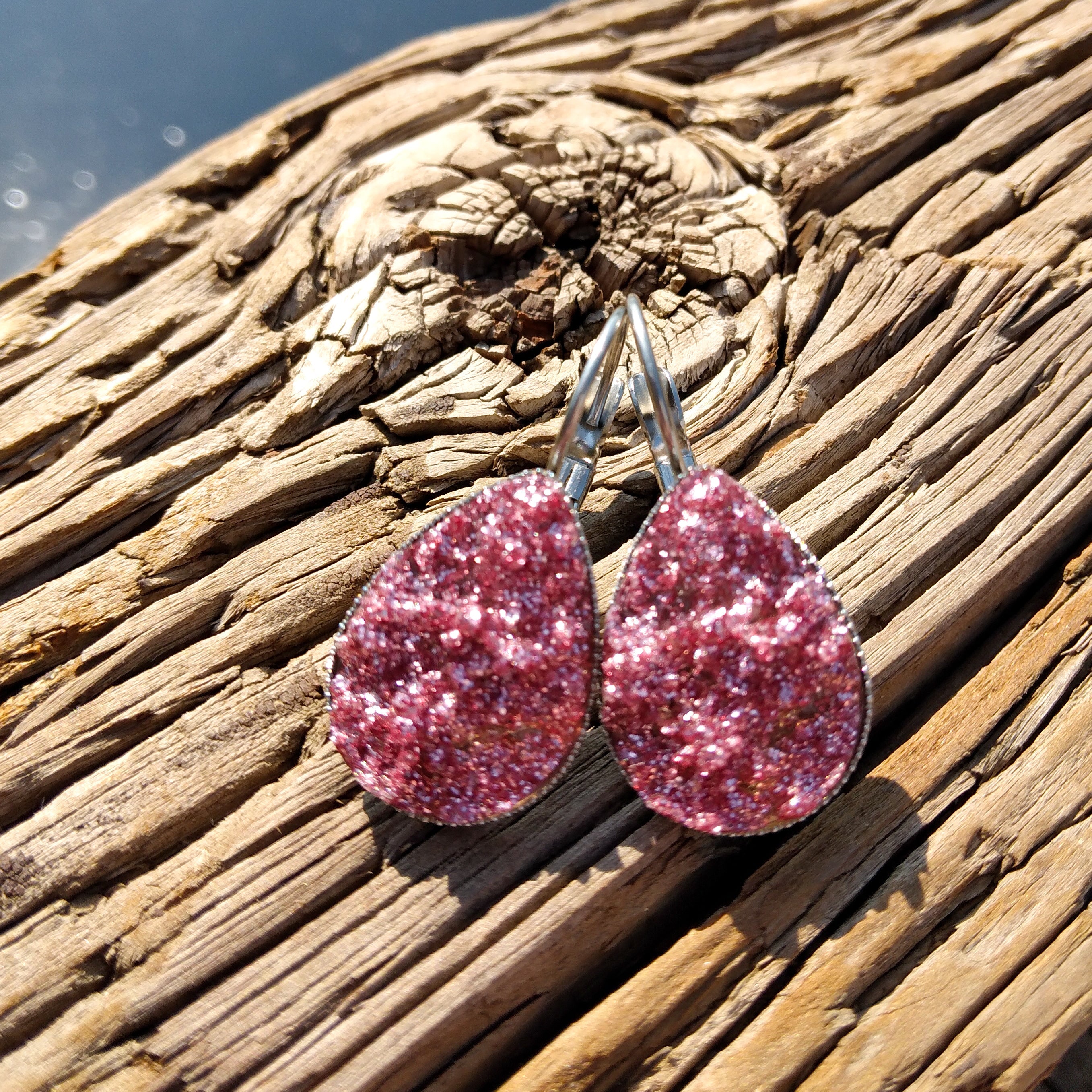 A pair of watermelon pink dangle earrings with a silver-tone metal setting, displayed on a wooden surface.