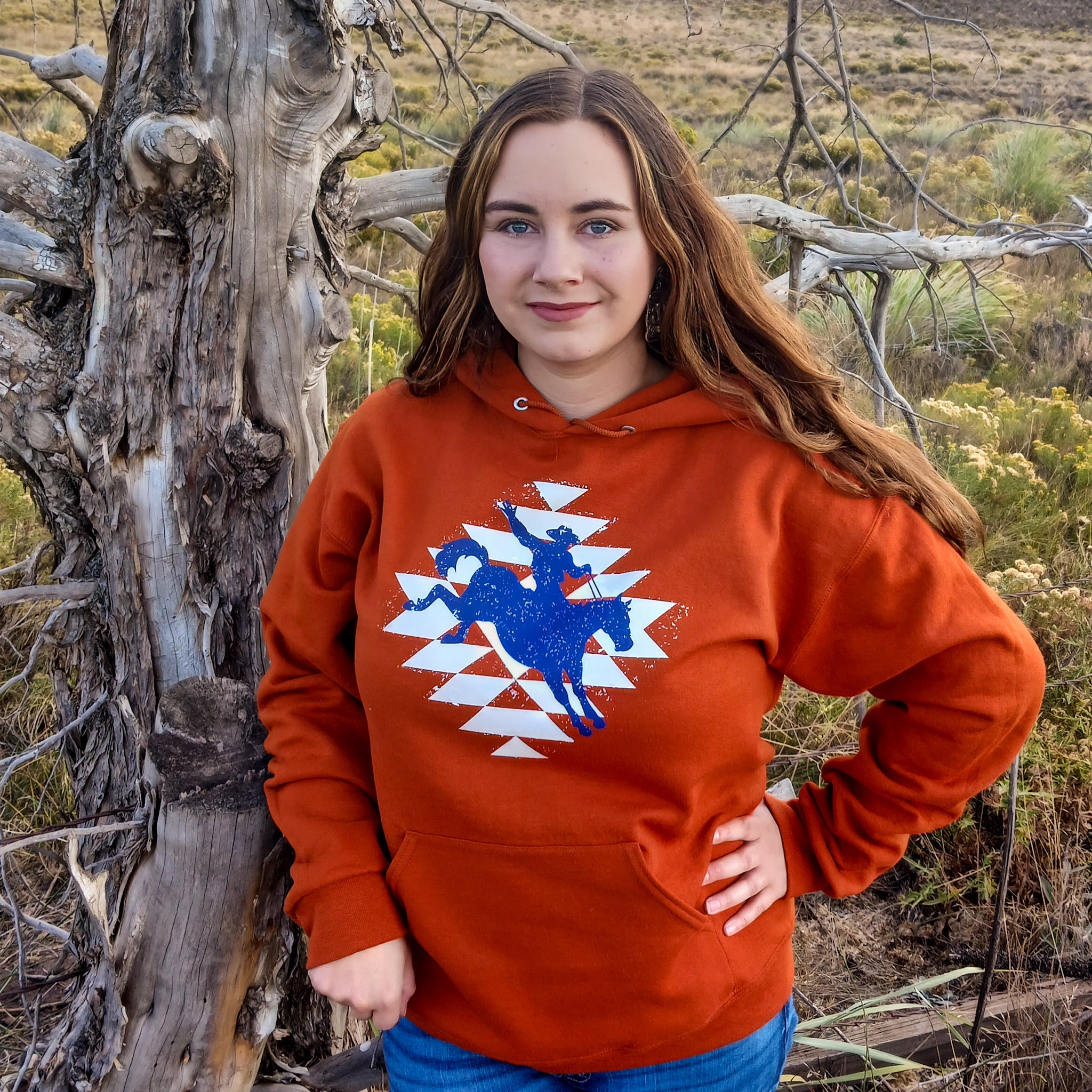 Cowgirl wearing an orange hoodie with a cowboy western graphic design in a ranch setting