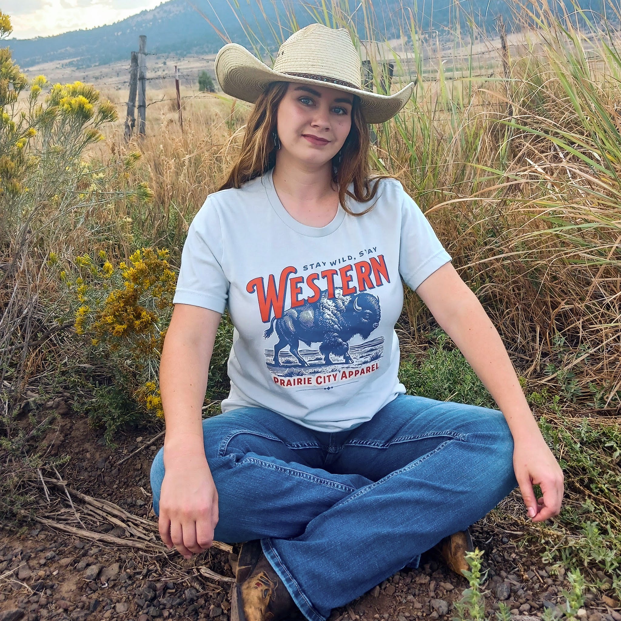 Person wearing a 'Western' t-shirt and cowboy hat sitting in a natural setting.