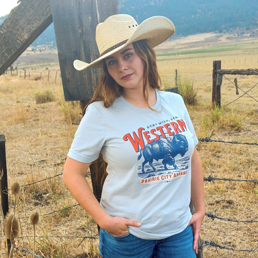 Woman wearing a cowboy hat and a t-shirt with a Western design in a rural setting.