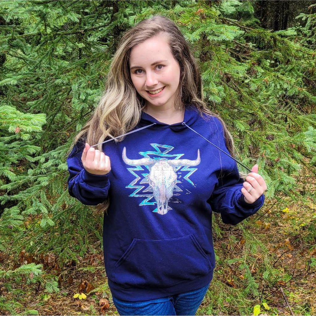 Cowgirl wearing a navy blue Western Aztec bull skull hoodie with a nature background