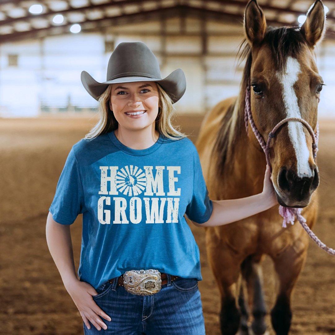 Cowgirl wearing a Blue Home Grown Homesteading Wester graphic tee while holding a horse in an arena