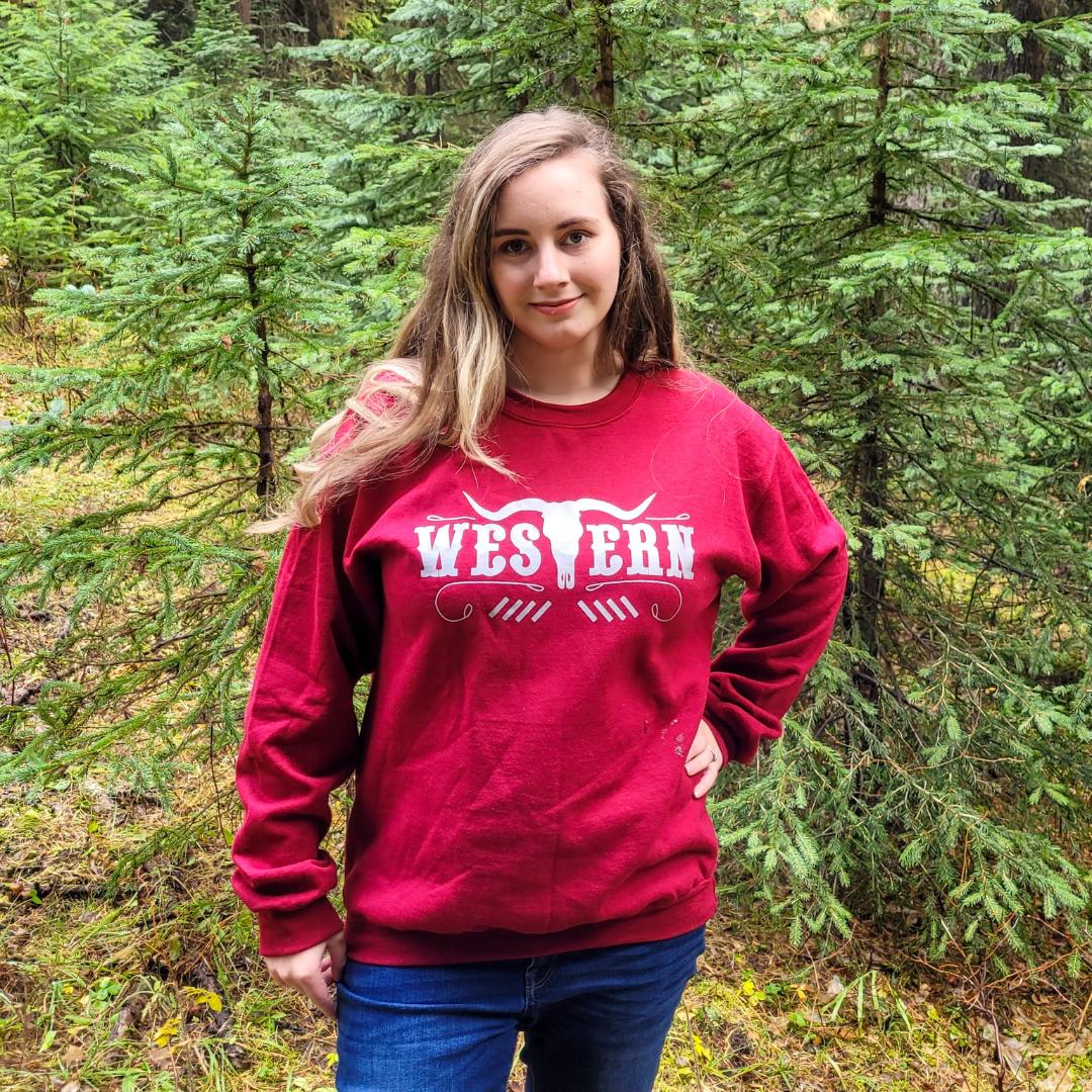 Woman wearing a red crewneck sweatshirt that has a long horn bull with the words “western” in silver across it